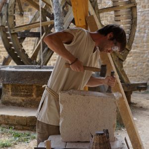 4--Guedelon---Tailleur-de-pierre-dans-la-cour-du-chateau-avec-le-puits-et-la-cage-a-ecureuil-en-arriere-plan