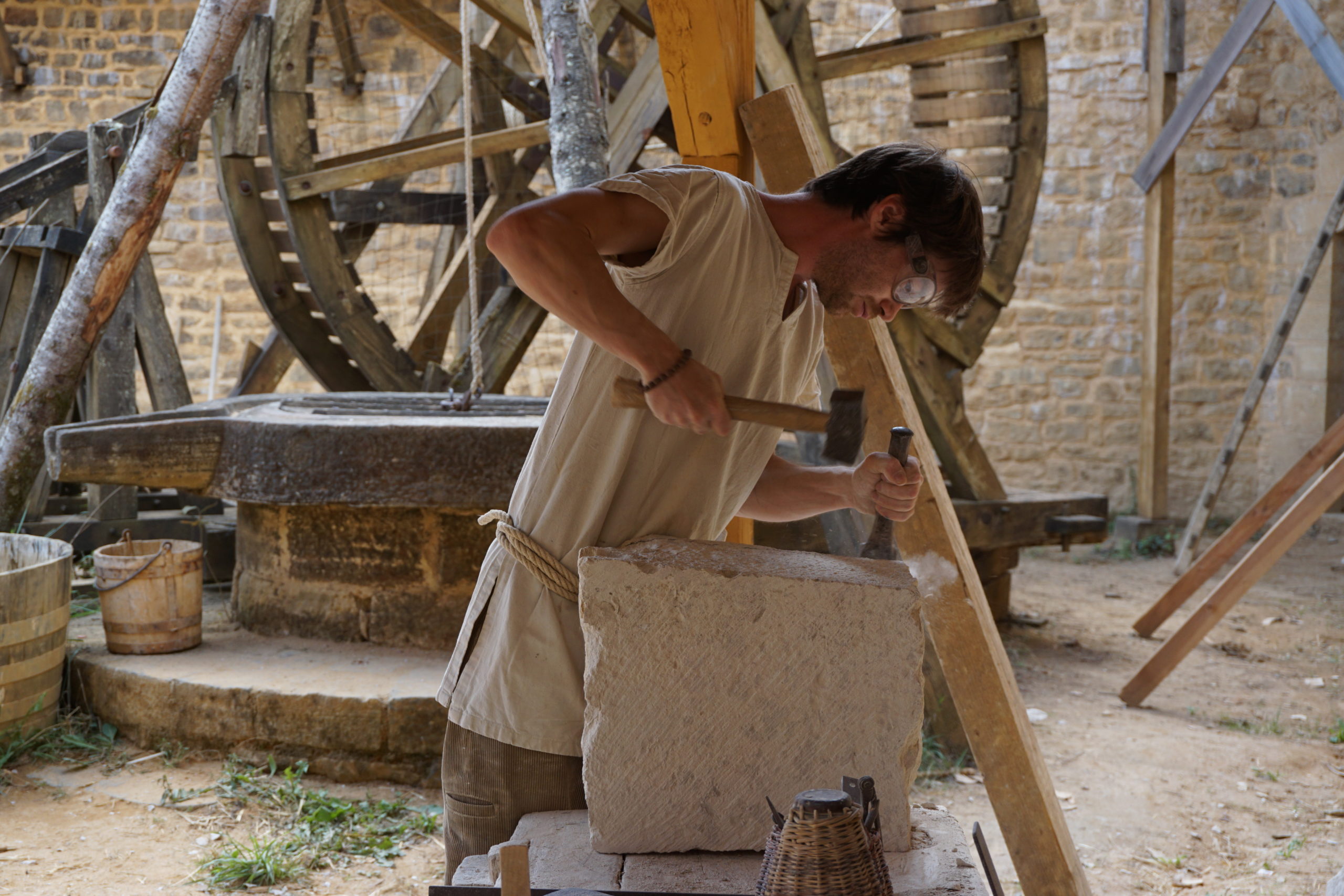 4--Guedelon---Tailleur-de-pierre-dans-la-cour-du-chateau-avec-le-puits-et-la-cage-a-ecureuil-en-arriere-plan